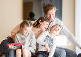 Eine glückliche Familie bestehendv aus zwei Erwachsenen und zwei Kindern im Wohnbereich einer Ferienwohnung