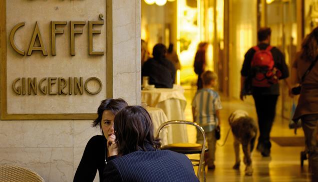 Persone parlano davanti al Caffè Gingerino a Bolzano, sullo sfondo passanti sotto i portici.